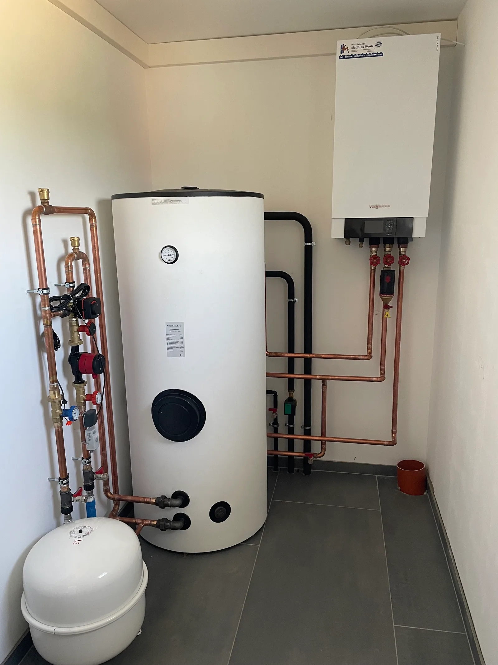 Wandhängende Gastherme mit dem Aufkleber Installationen Matthias PAAR, daneben ein Warmwasserspeicher