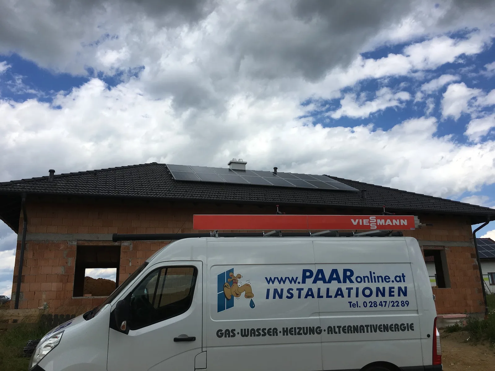 Firmenwagen mit der Beschriftung PAARonline.at Installationen vor einem Rohbau mit fertiger Photovoltaik-Anlage
