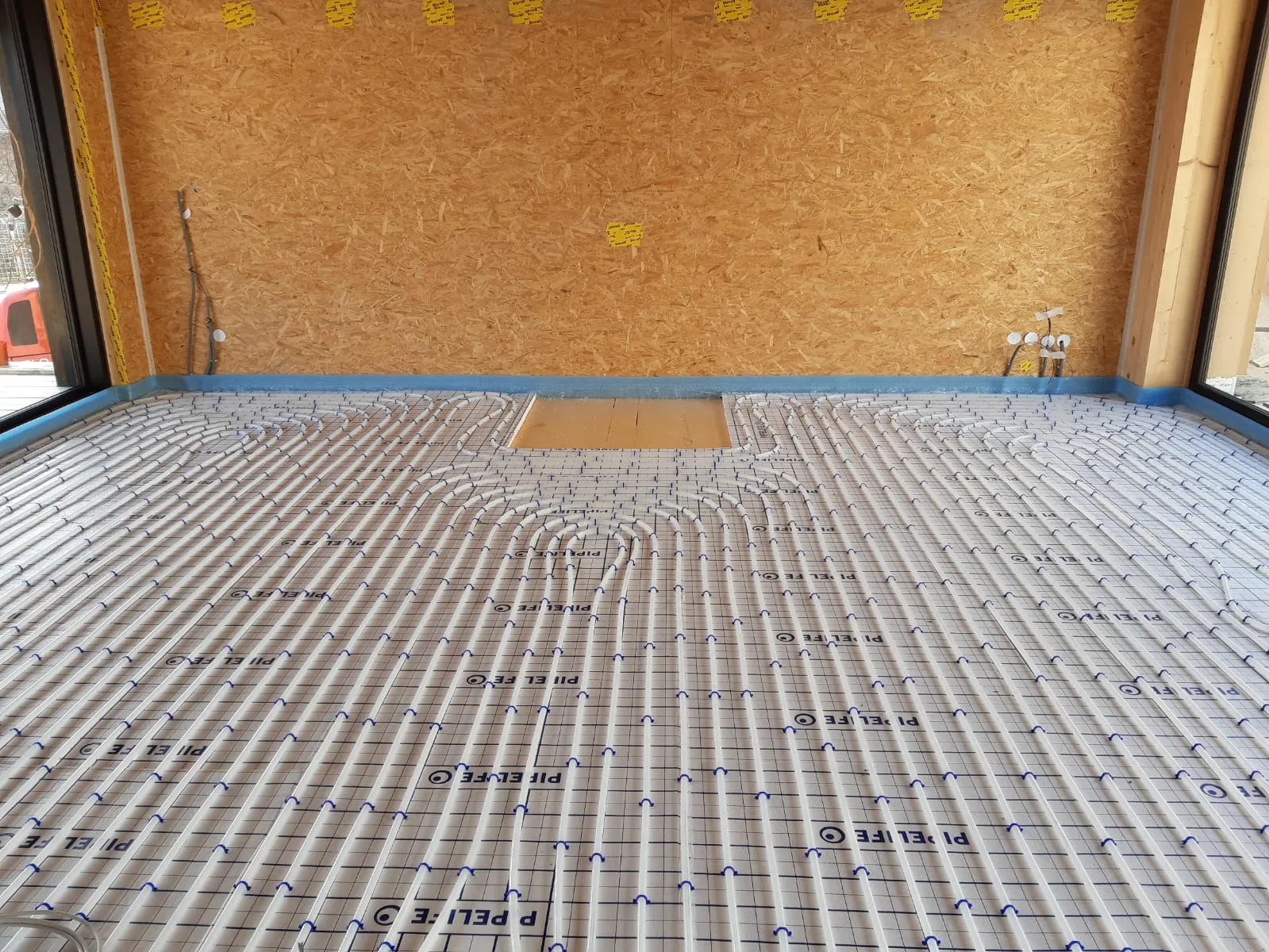 Verlegte Fußbodenheizung mit weißen Rohren auf einer Tackerplatte in einem Holzbau-Rohbau