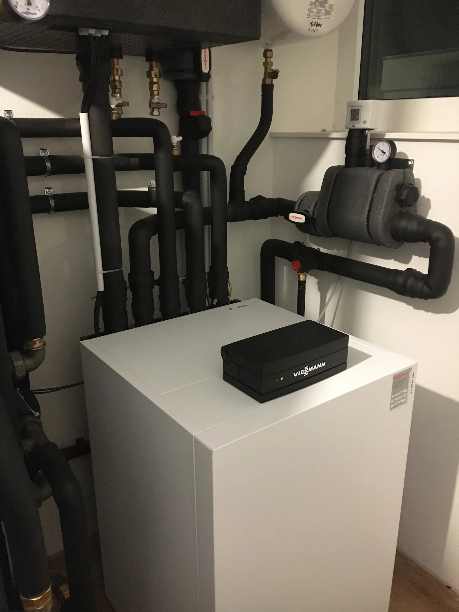 Weiße Wärmepumpe im Heizraum, daneben ein Pufferspeicher mit schwarz gedämmten Leitungen